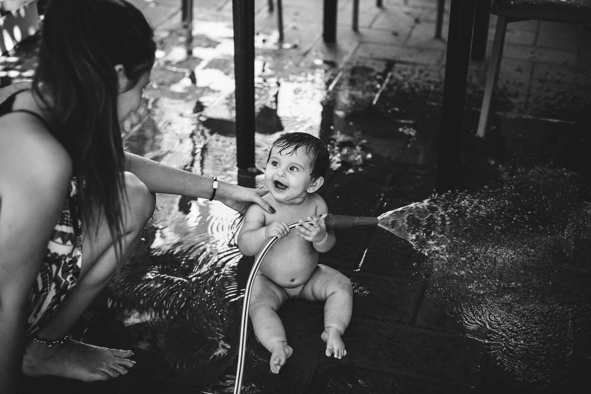 Baby playing with water, with her older sister at the backyard of their house. Black and white picture. Amsterdam documentary photoshoot.