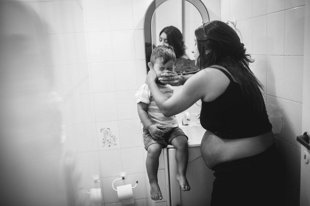 Photo of a pregnant mom cleaning her toddler face in the bathroom. Natural style of maternity photography in Amsterdam.