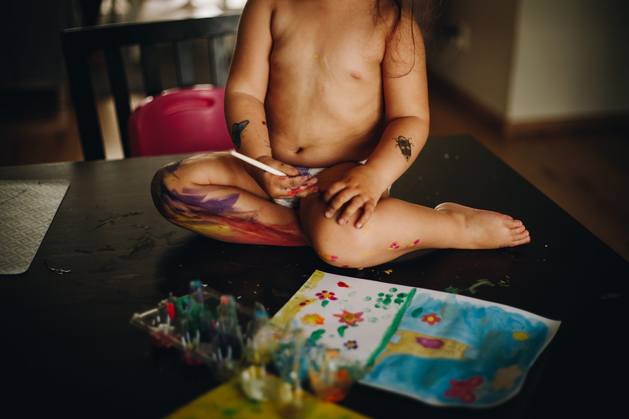 Girl painting herself with tempera sitting on the dinner table. Amsterdam.