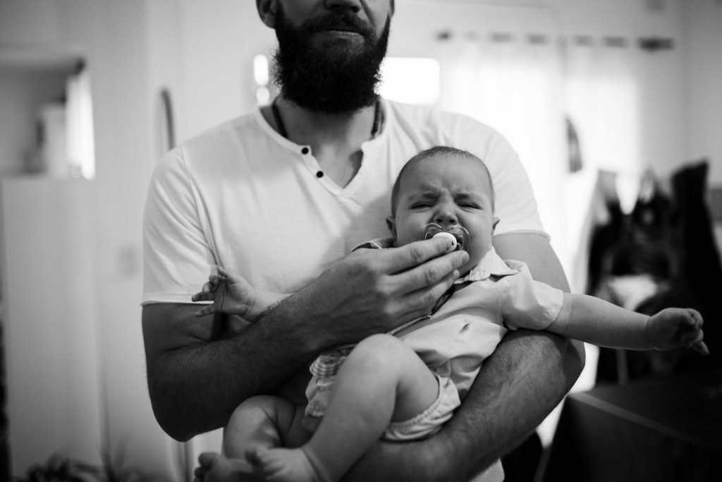 Dad holding pacifier in baby's mouth trying to confort him while he cries. Family photographer in Amsterdam, Netherlands.