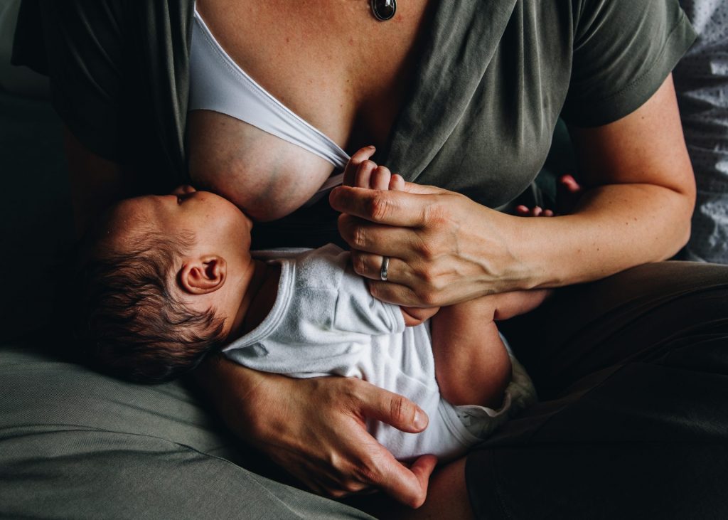 mom breastfeeding her newborn while holding his little hand. love, conection, respectful parenting. Documentary family photographer in Amsterdam area.