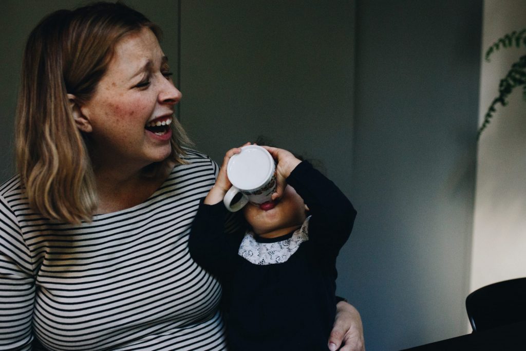 mom laughing while her toddler is drinking yogurth