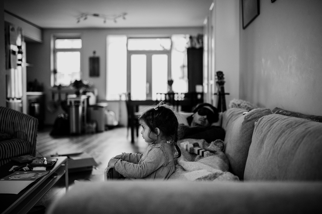 little girl watching TV while her father is sleeping next to her