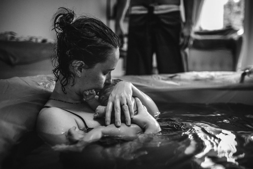 gentle home birth - mom holding and kissing her newborn child inside the birth pool