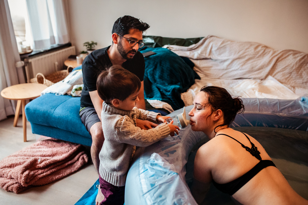 child giving water to his mom while she's in labor of her second child.