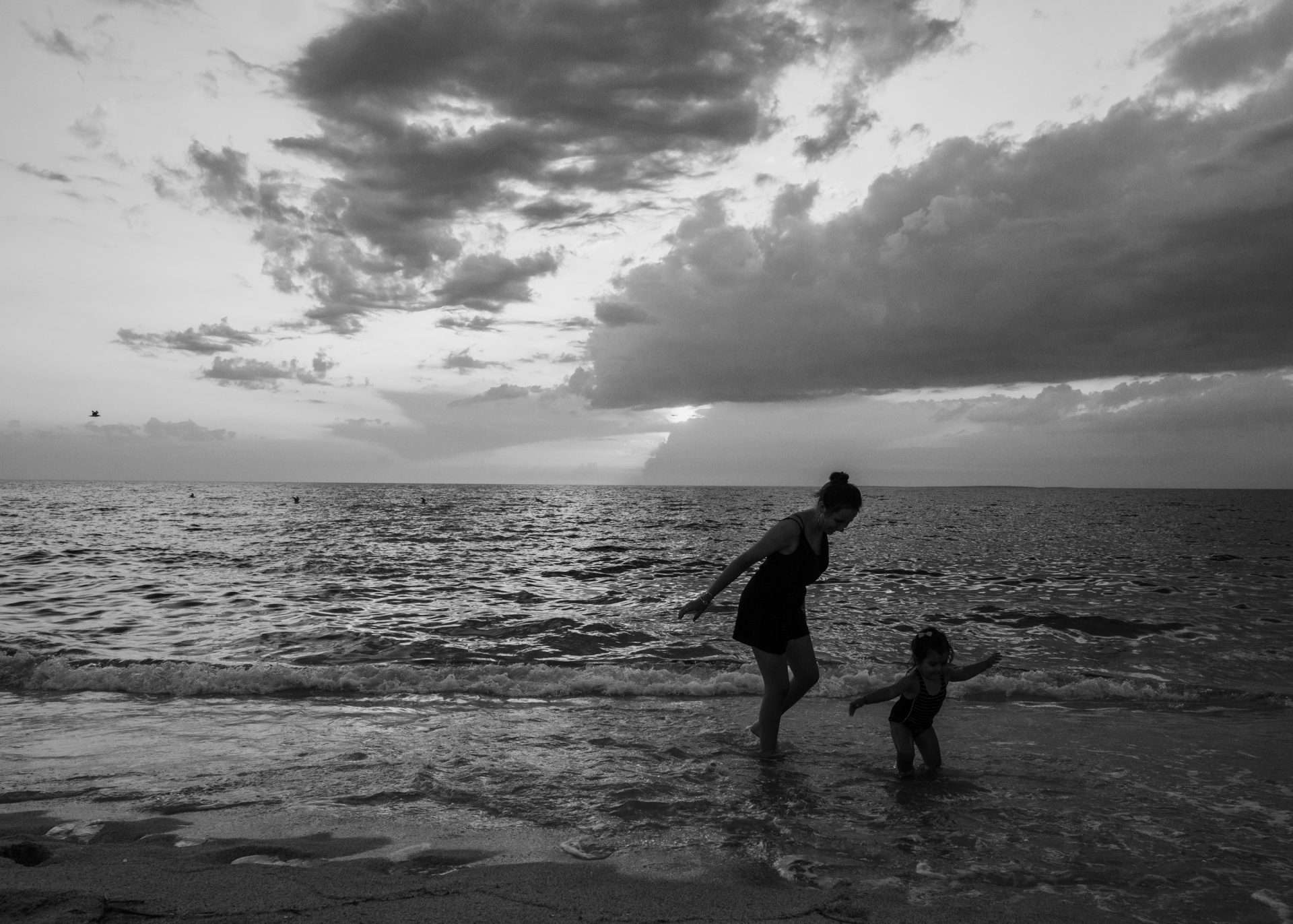 Two girls, one teenager and the other is a todler, running on the beach on a Sunset afternoon. Cerdegna, Italy. Black and white picture. Documentary style.