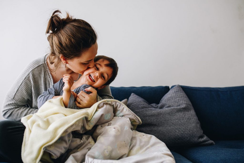 happy moment in the living room. Mom is kissing her toddler. The kid is laughing