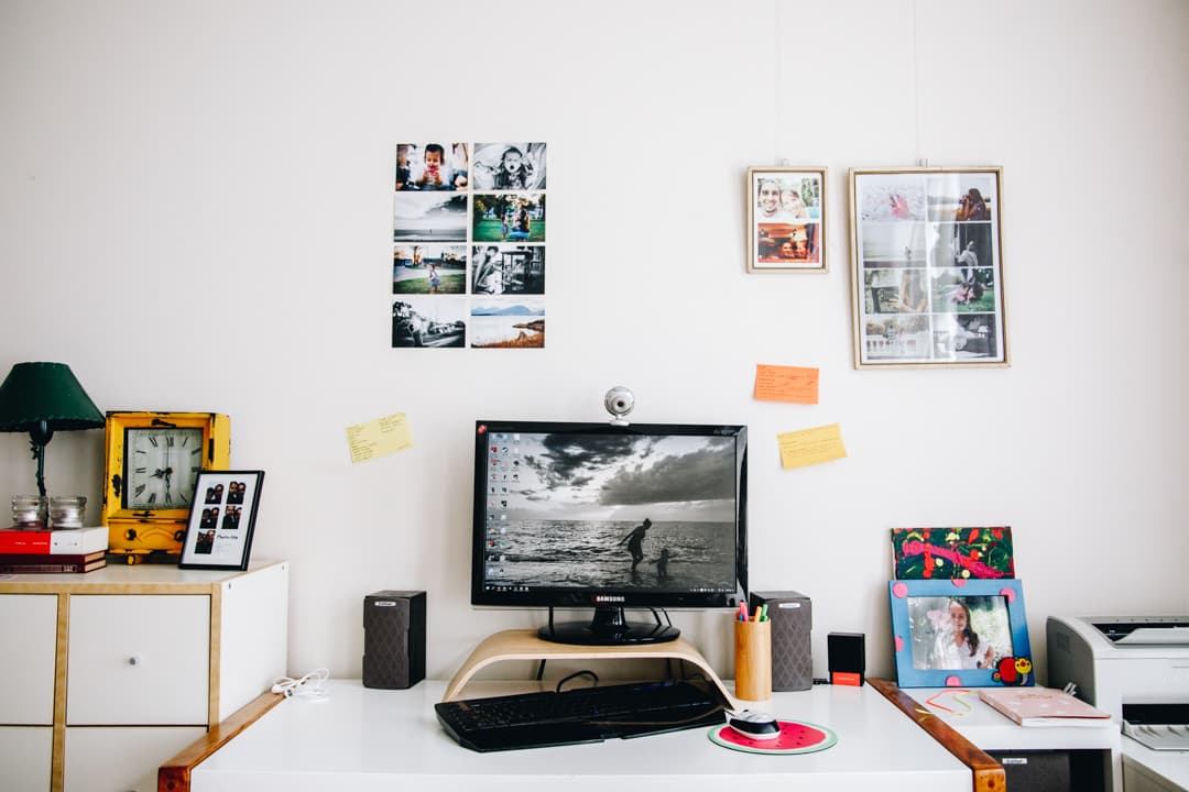 Computer desk displaying a photo of two girls runing on the beach (the photo is in black and white). Also, on the wall behind the screen you can see family photos hanging