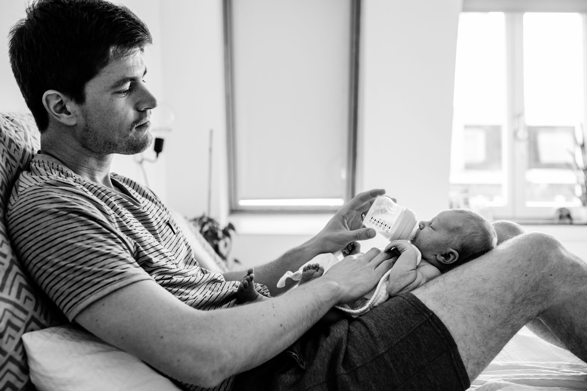 Dad feeding with bottle his newborn child, while baby is laying on his lap