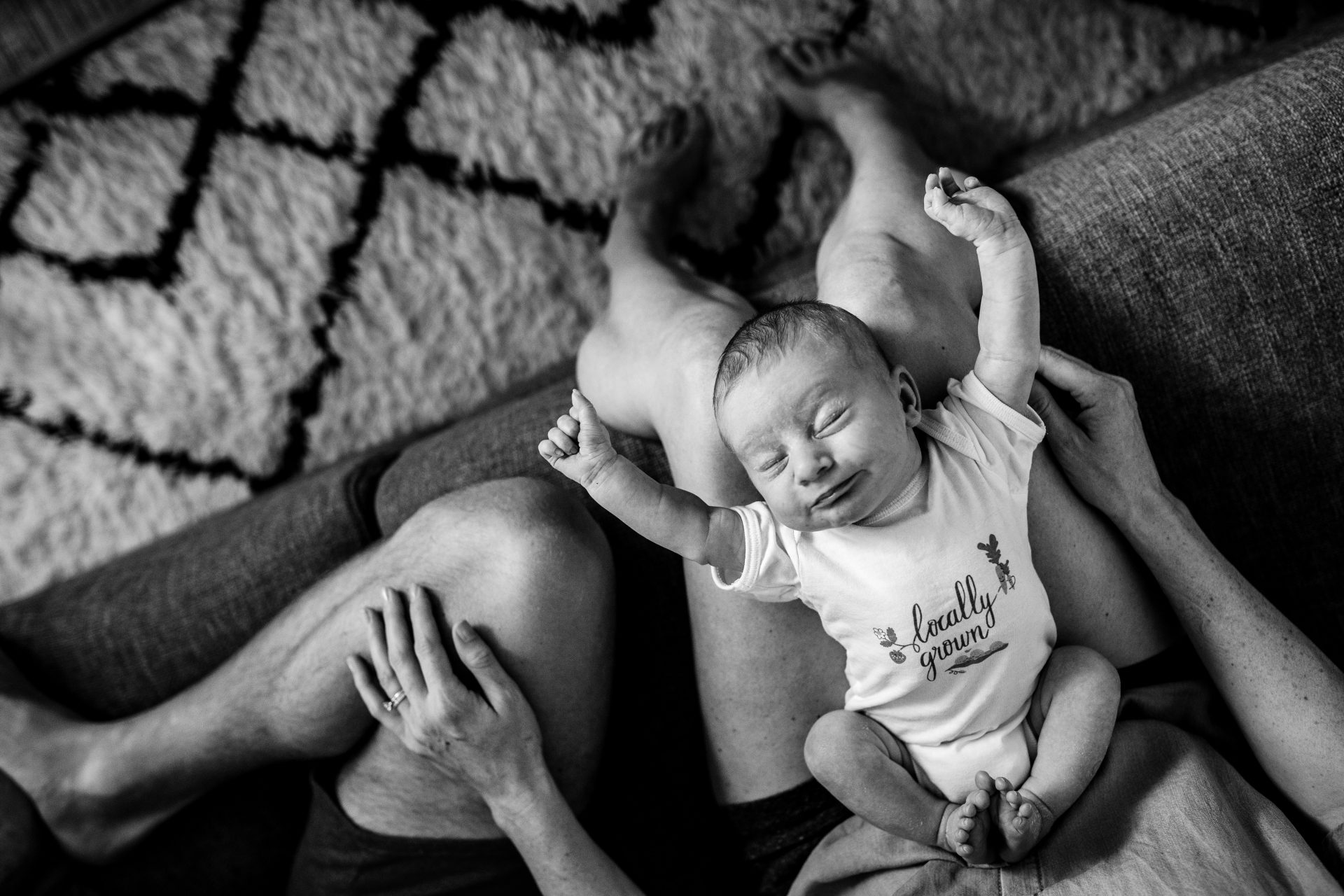 newborn stretching her arms on, lying on the lap of her mom. Black and white picture.