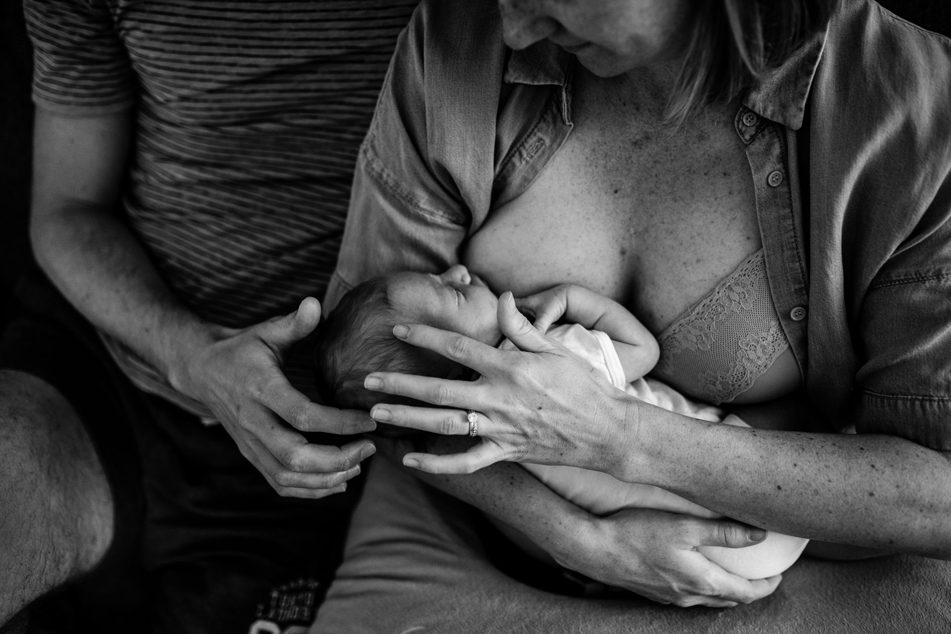 newborn latching her mom's breast, while being caressed by both her parents. Black and white picture.