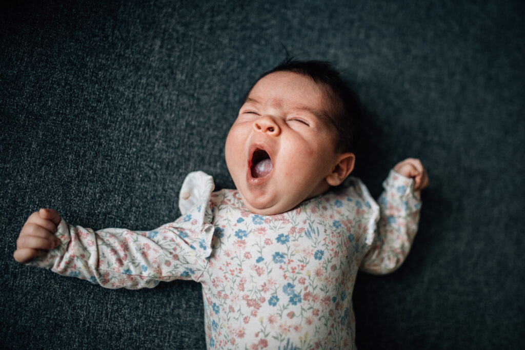 Newborn portrait. The baby is lying on a blue sofa, giving a big, beautiful yawn.