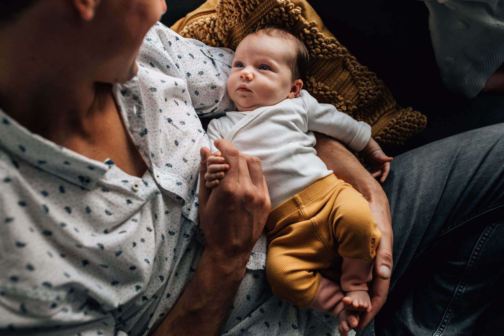 Portrait of a newborn baby being hold by her dad on his lap. Baby girl contemplating at him, while holding his hand.