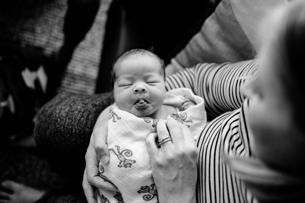 Black and white portrait of a newborn baby making faces at his mother while in her lap