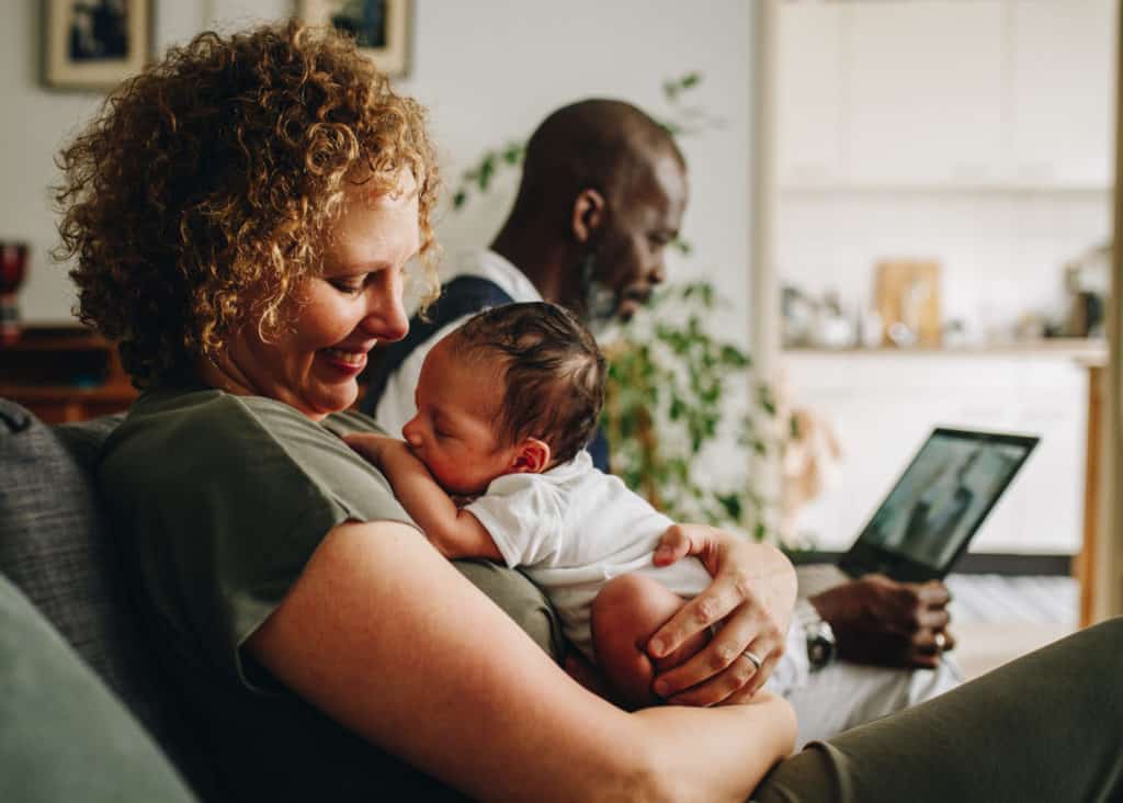 newborn nestling on mom's chest. She's looking at him happy, with a smile. Dad is behind them working on his computer. Amsterdam, Netherlands.
