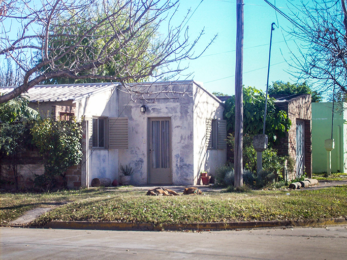 Front view of my childhood's home in Argentina. My dogs are lying on the grass. Windows are open. Sky is blue.