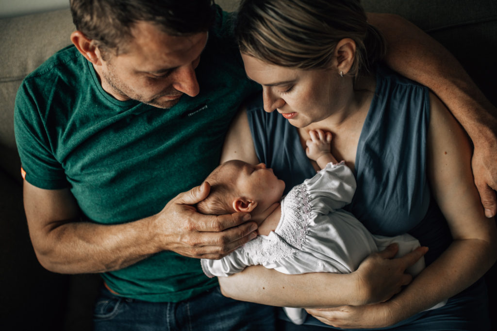 Family portrait with a newborn. Both mom and dad are glazing at their newborn baby while caresing her. Amsterdam newborn sessions at home.