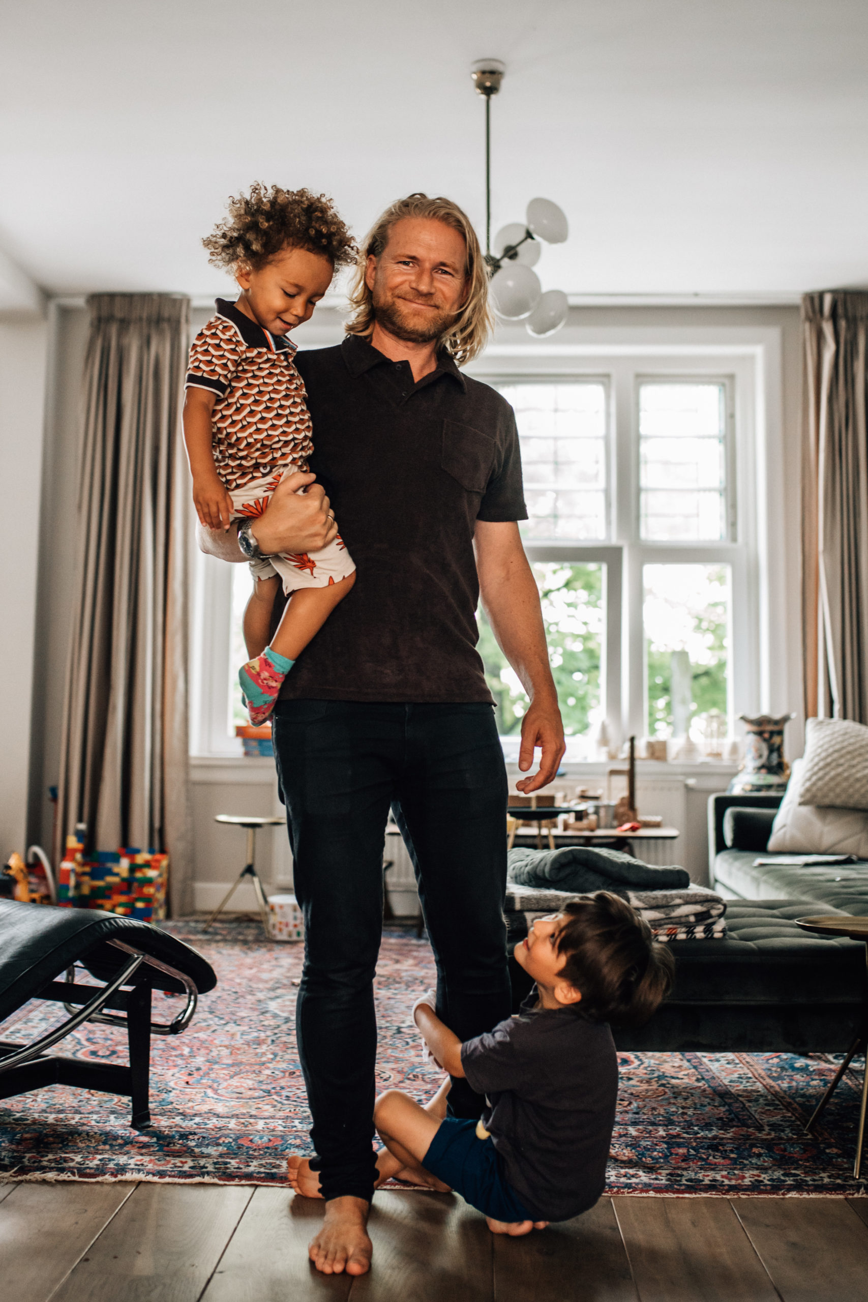 Father holding one of his children on his arms while the other kid is holding him from his legs