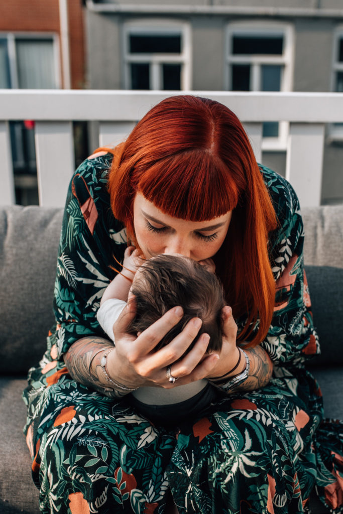 mom kissing her newborn baby on her cheek, holding her carefully