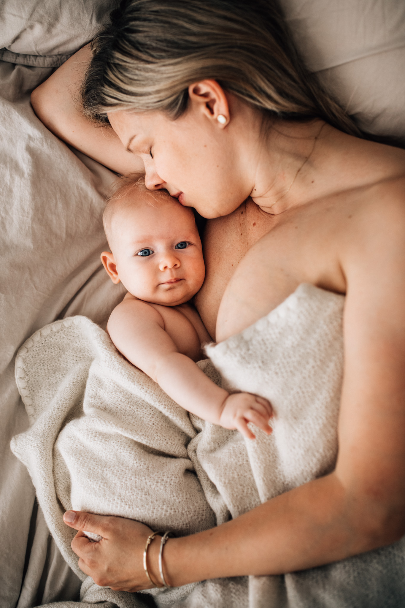 mom smelling her baby's head, both lying on the bed