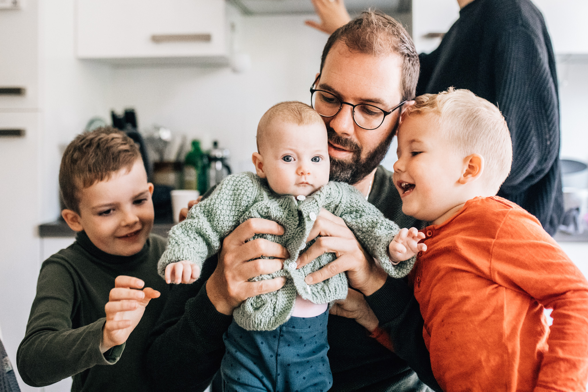 dad holding his newborn baby girl while his two older kids are next to them, smiling