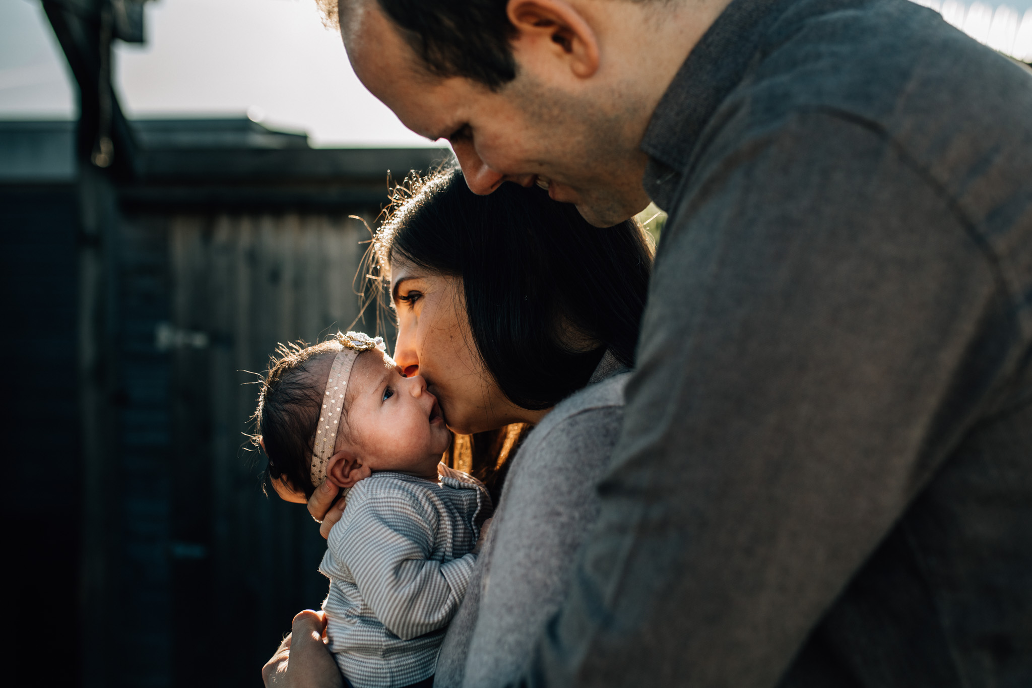 Outdoors photography. Mom holding and kissing her newborn girl while dad is hugging them