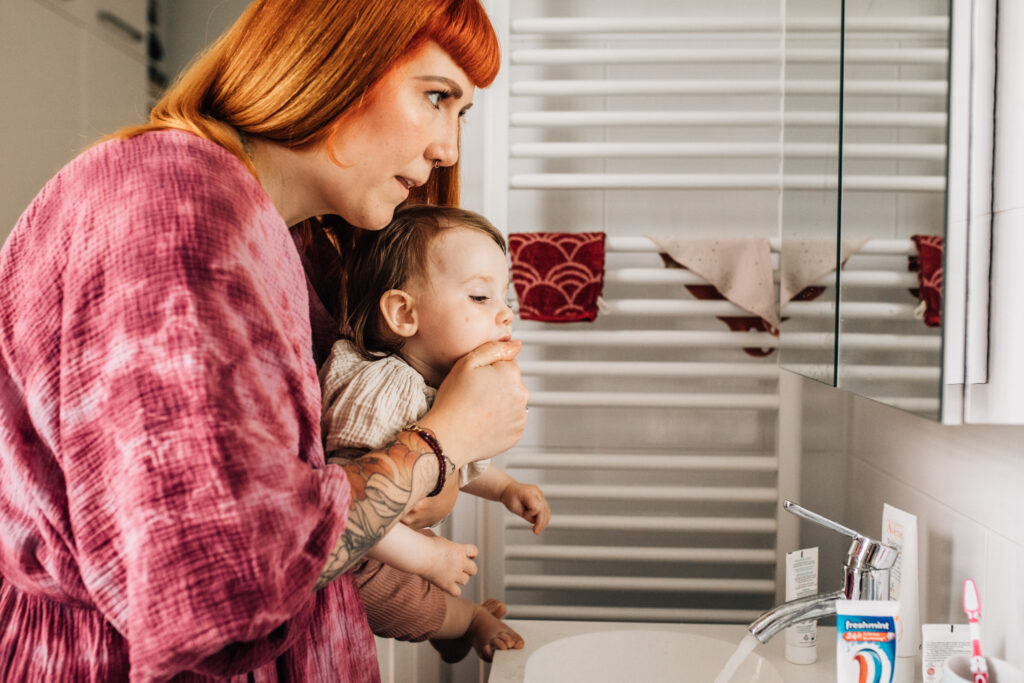 In this image, mom is holding her child in the badroom, washing her little one's face.