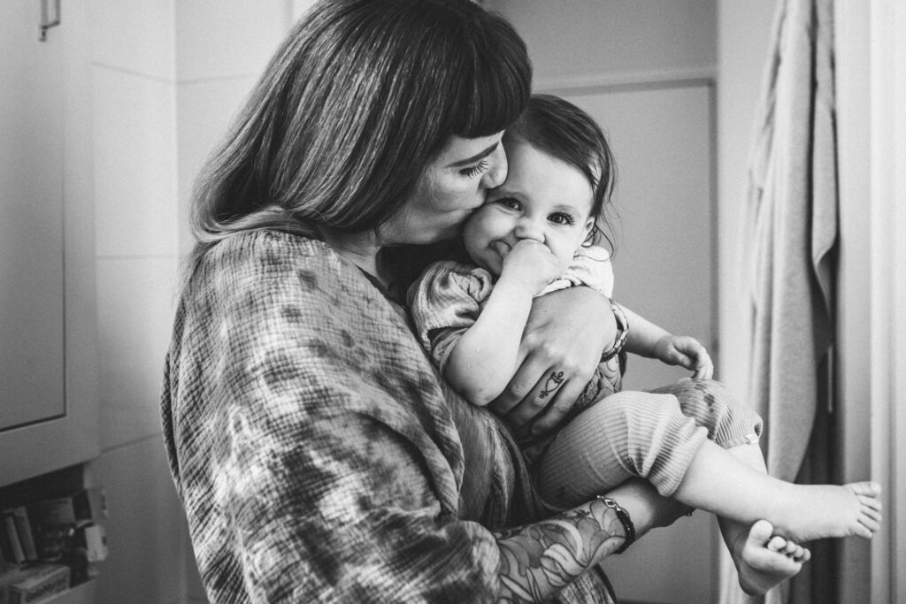 Black and white picture of mom holding her child and kissing her cheek after washing her face. The little one is looking at the camera.