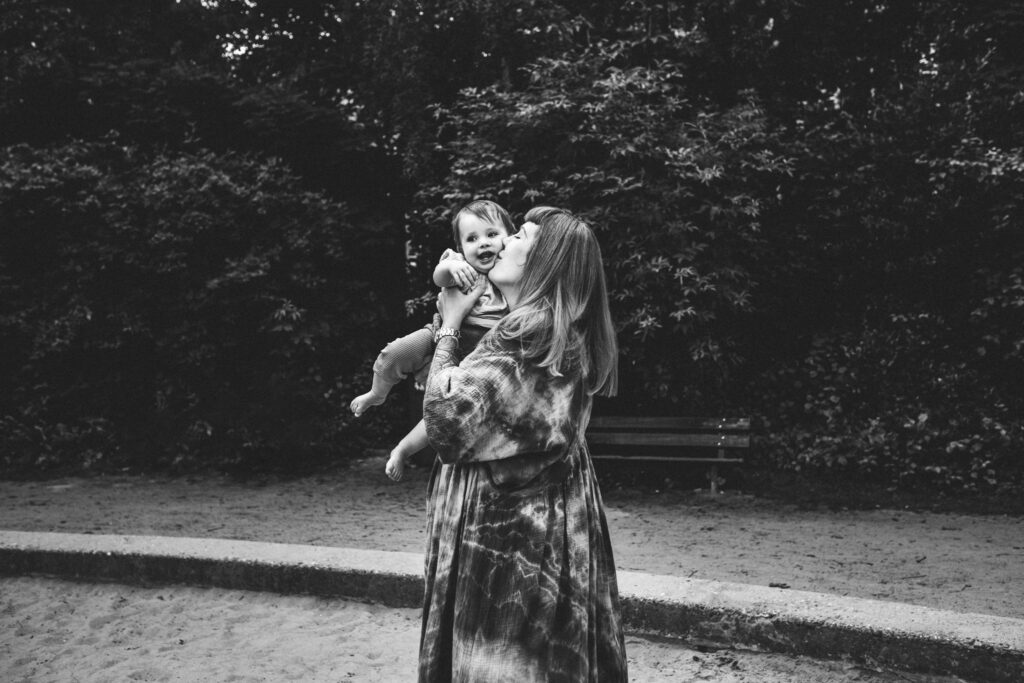 Mom kissing her little girl's cheek while holding her in the Sarphatipark. The little one is smiling.