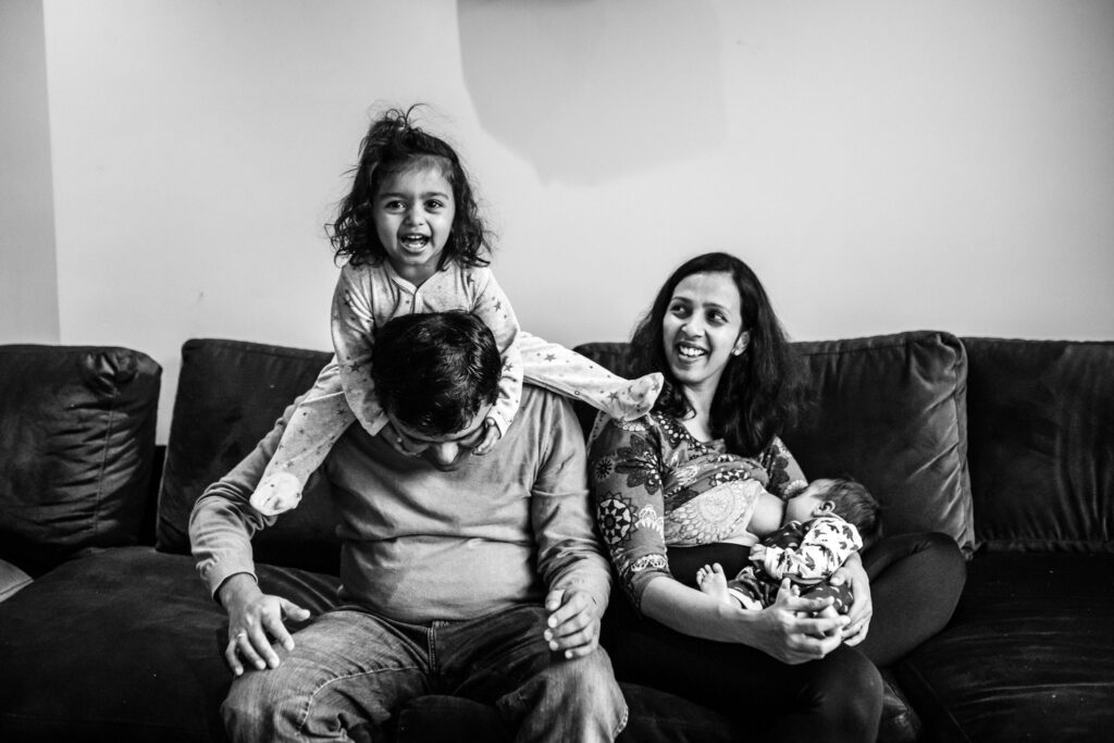 black and white family portrait of a mother holding her newborn child while breastfeeding and the father holding their tolder on his shoulders