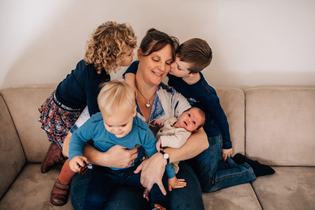 portrait of a mother holding her newborn while cuddling with her older 3 children