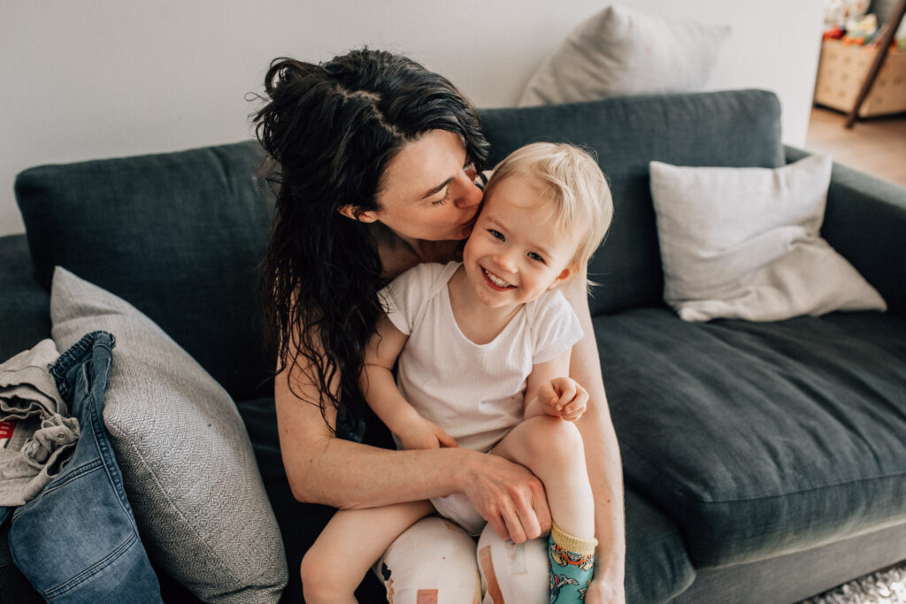 Amsterdam mom kissing her child on his cheek while they're sitting on the couch of their living room, in a family photography session at their home.