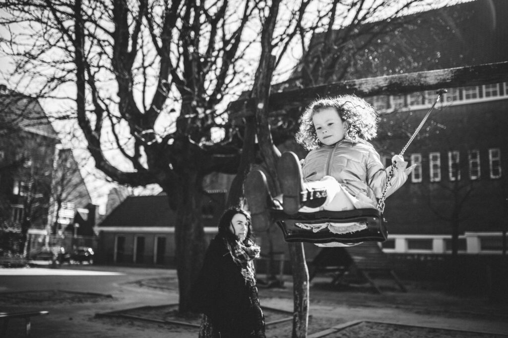 Mom looking at her daughter while the little one plays on the hammocks. Black and white photo, Amsterdam family photography.